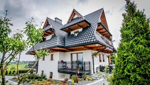 Een modern chalet met schuin dak, een balkon met zwarte leuning en een verzorgde tuin.