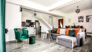 Een moderne woonkamer met een grijze bank, een groene fauteuil en een trap naar een hoger niveau.