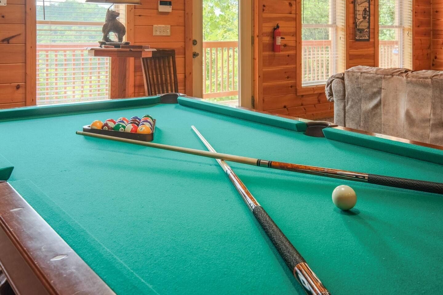 A pool table with balls and cues, a wooden chair, and a statue in the background.