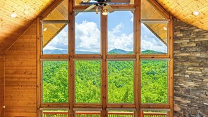 Ein Zimmer mit großen Fenstern und Blick auf einen bewaldeten Gebirgszug.