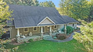A two-story house with a stone foundation, a covered porch with chairs, and a well-maintained lawn. - Luxury getaway. 5 BR, 3BA, 3500 sq. Ft., 2 acres. Sleeps16. (West Olive)