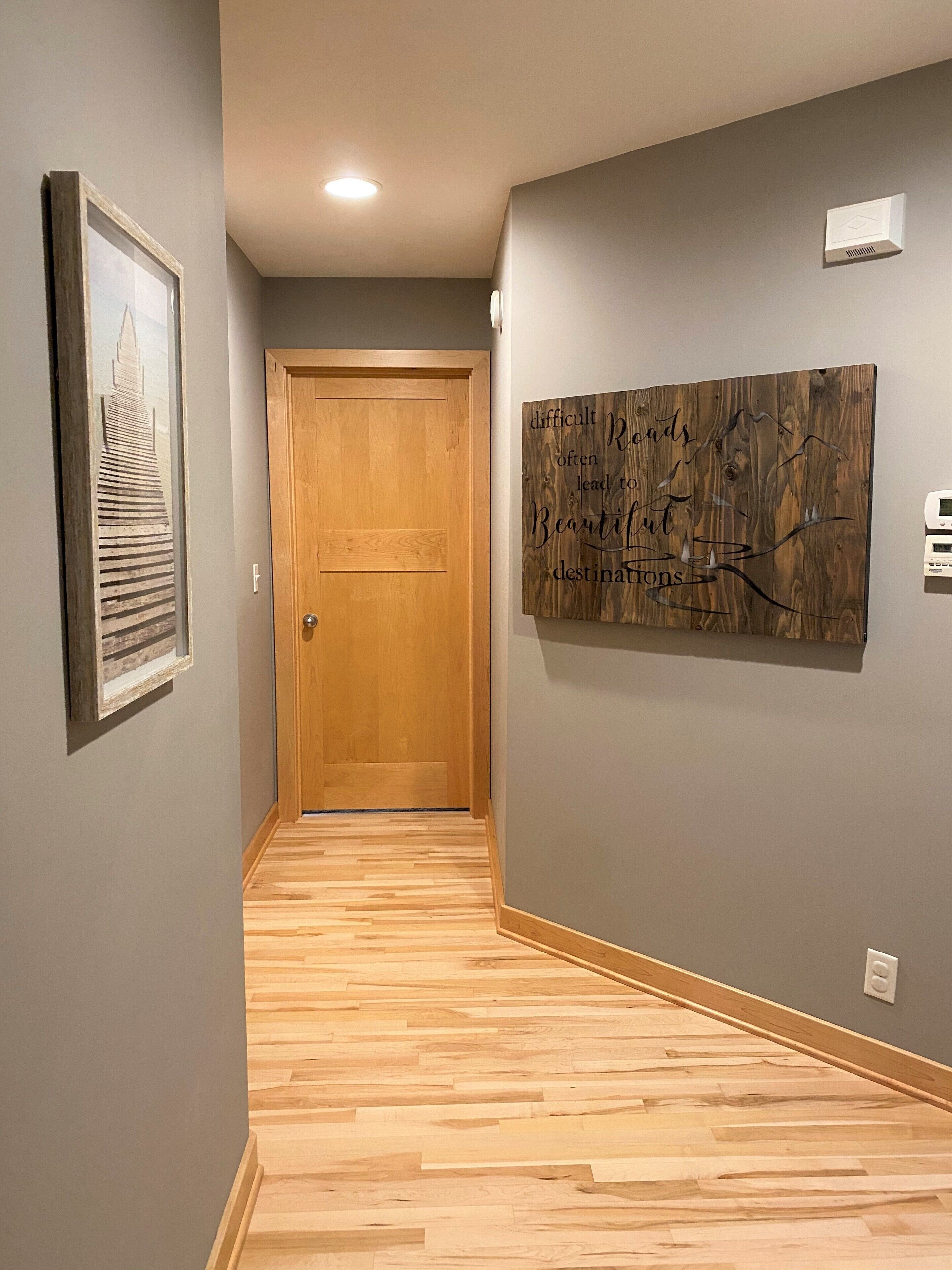 A hallway with a wooden door, a framed picture on the left, and a large abstract painting on the right.