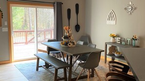 A dining area with a wooden table and benches, a rug, and a view through a glass door to an outdoor deck. - Luxury getaway. 5 BR, 3BA, 3500 sq. Ft., 2 acres. Sleeps16. (West Olive)