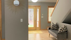 A modern living room with a grey sofa, patterned cushions, a sunburst mirror, and a wooden floor. - Luxury getaway. 5 BR, 3BA, 3500 sq. Ft., 2 acres. Sleeps16. (West Olive)