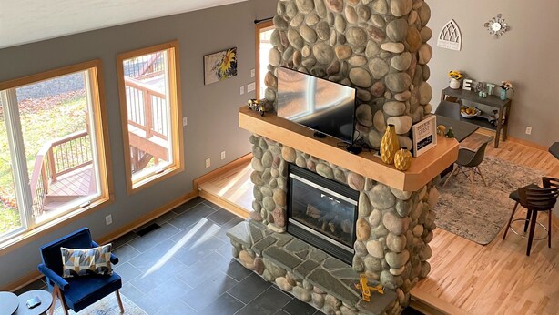 A living room with a stone fireplace, large windows, and a view of the outdoors. - Luxury getaway. 5 BR, 3BA, 3500 sq. Ft., 2 acres. Sleeps16. (West Olive)