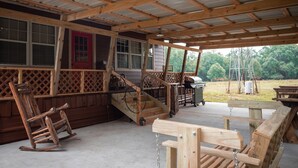 Une véranda couverte avec des meubles en bois, un fauteuil à bascule et un barbecue.