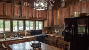 Une cuisine rustique avec des meubles en bois, un réfrigérateur noir, une cuisinière et une table à manger ornée d’une statuette de cochon.