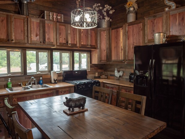 A rustic kitchen with wooden cabinets, a black refrigerator, a stove, and a dining table with a pig figurine. - Rustic Cabin in the Woods (Needville)