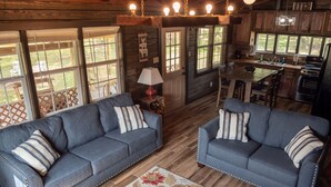 L’intérieur d’un chalet accueillant, avec deux canapés gris, un plancher en bois et un coin cuisine.