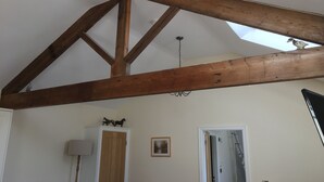 Ein Zimmer mit schrägem Dach, Holzbalken, einem Oberlicht, einer Kristallleuchter, einem Kleiderschrank und einer Tür zu einem anderen Raum.