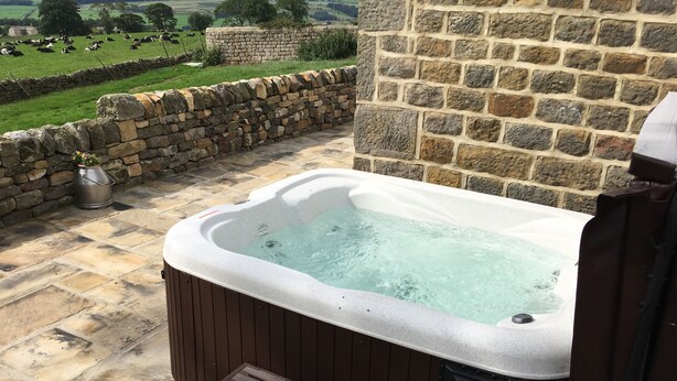 Ein Whirlpool mit Steinwand, einem Steinweg und Blick auf ein grünes Feld mit Kühen.