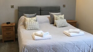 Ein ordentlich bezogenes Bett mit grauem Kopfteil, zwei Nachttische mit Lampen und ein gerahmtes Bild an der Wand.