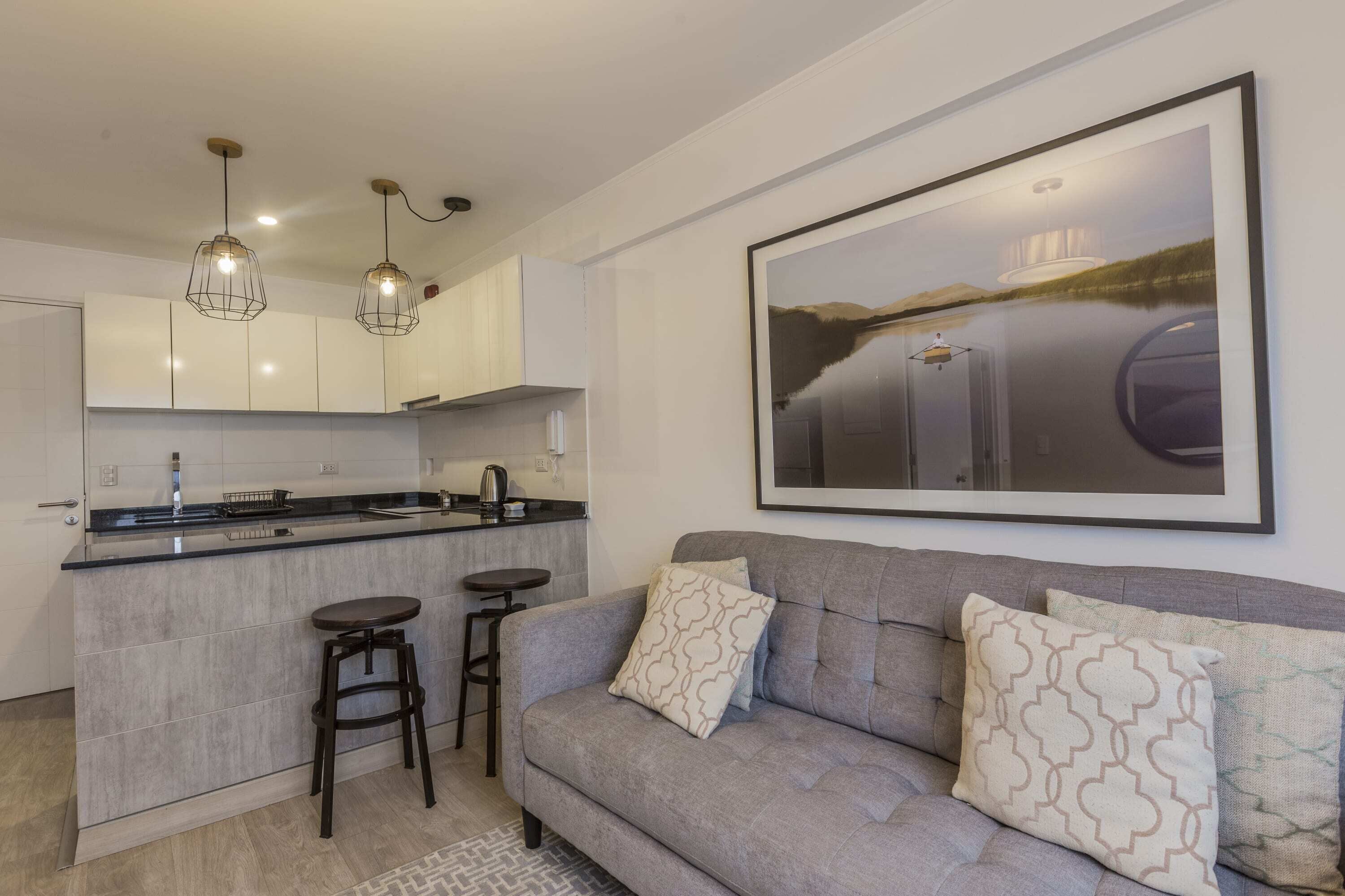A modern kitchen with a central island, bar stools, pendant lighting, and a large framed picture on the wall.