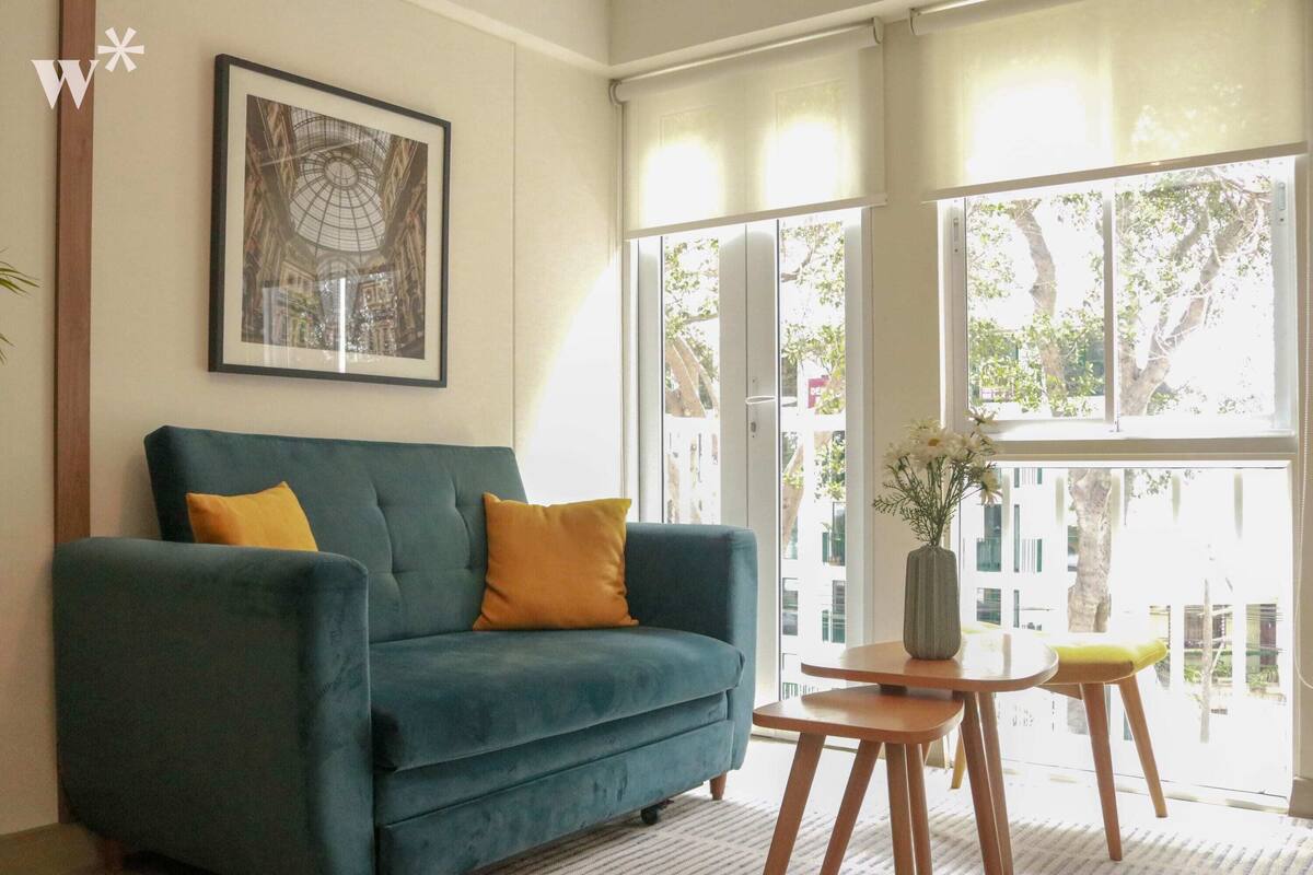 Uma sala de estar com um sofá azul, uma mesa de madeira pequena e um quadro na parede.