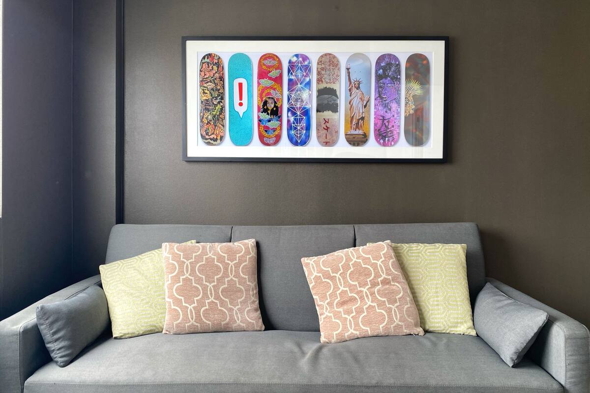 Um sofá cinzento com almofadas estampadas e uma obra de arte emoldurada de skateboards na parede.