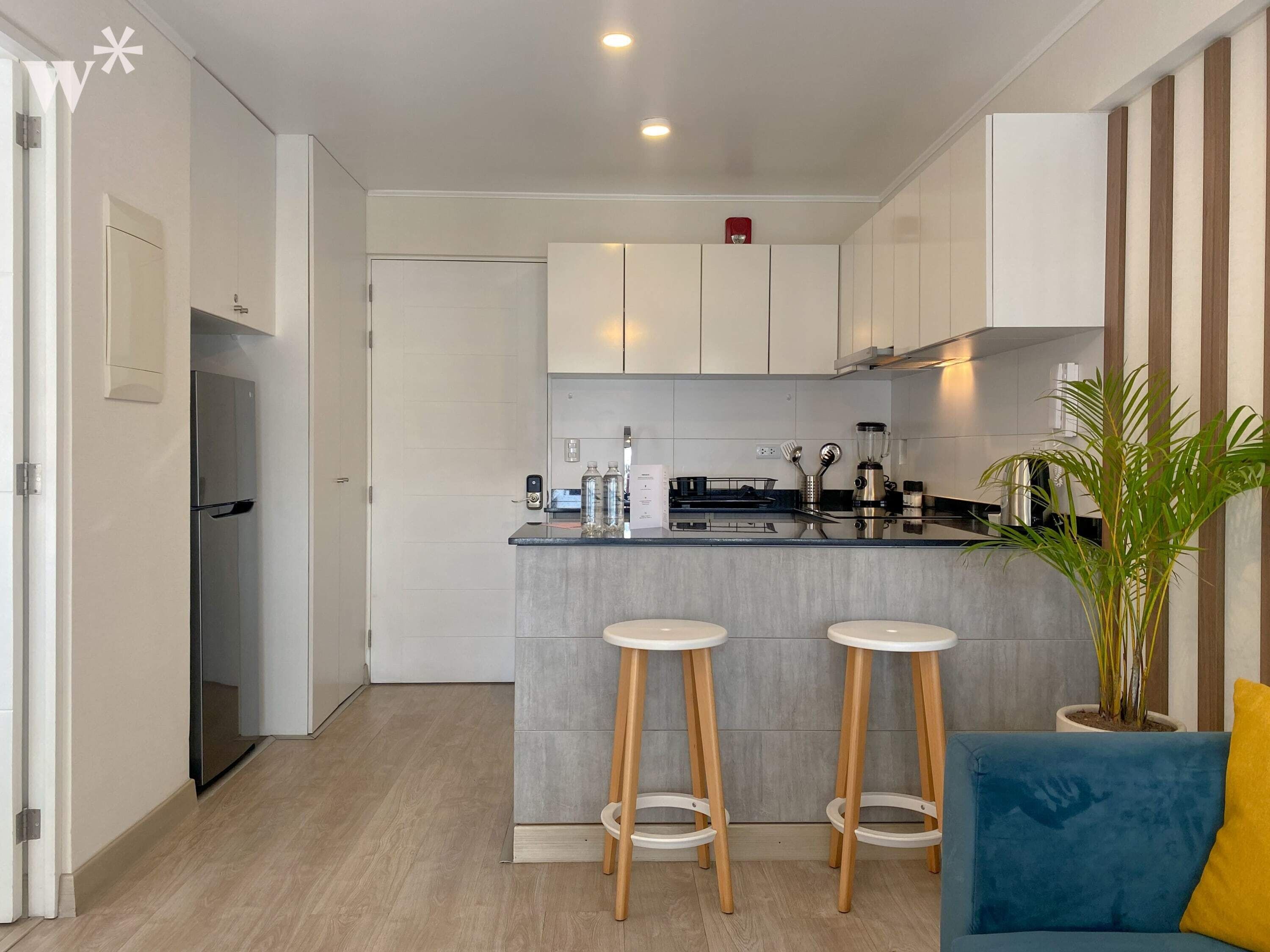A modern kitchen with a central island, two stools, a blue sofa, and a potted plant.