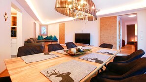A modern dining area with a long wooden table, black upholstered chairs, and a chandelier. - Mountain Living Apartments - Ski-In & Ski-Out (See)