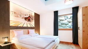 A bedroom with a wooden bed, a nightstand, a wall-mounted artwork, a window with curtains, and a wooden wardrobe. - Mountain Living Apartments - Ski-In & Ski-Out (See)