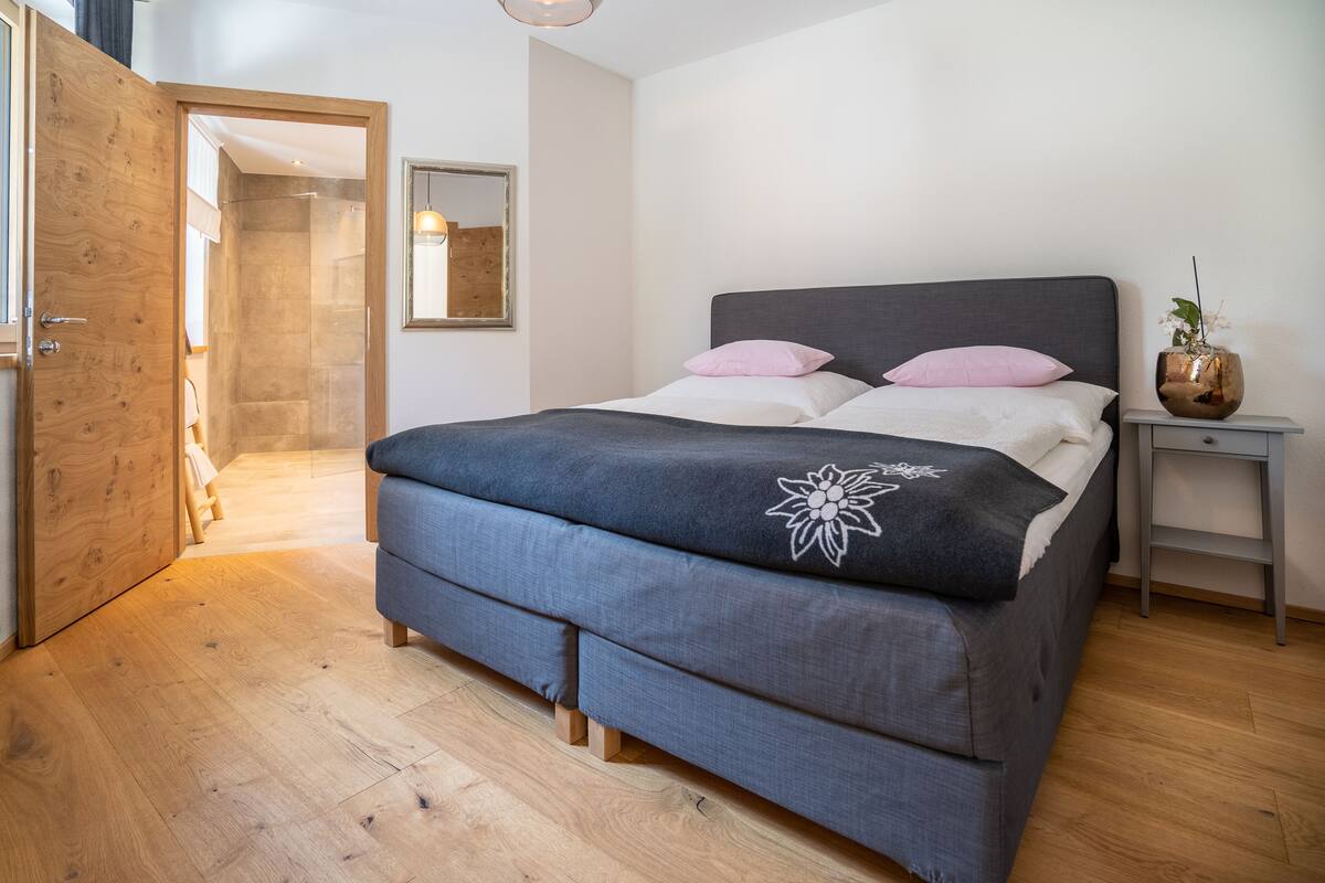 A bedroom with a bed, a nightstand, a mirror, and a wooden door.