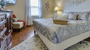 Une chambre à coucher avec un grand lit, une commode, un téléviseur et une fenêtre avec des rideaux.
