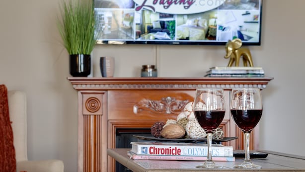Une cheminée agrémentée d’objets décoratifs, un téléviseur affichant un site web et deux verres de vin rouge posés sur une table.