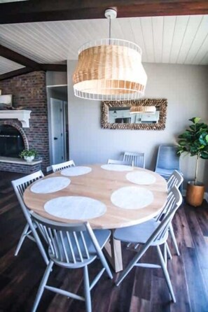 Un tavolo da pranzo rotondo in legno con tovagliette bianche, circondato da sedie in metallo, illuminato da una lampada a sospensione in fibra naturale.