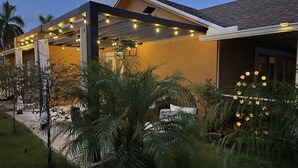 A modern house with a covered patio area, palm trees, and string lights. - Make yourself at home in Delray Beach!!<br><br><br> (Delray Beach)