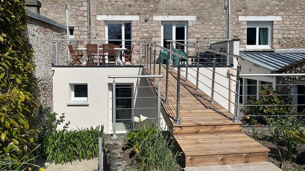 Un edificio de varios pisos de piedra con una terraza de madera y zona de estar al aire libre.