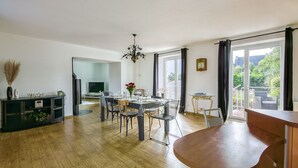 Un comedor amplio con una mesa y sillas de madera, una lámpara de araña y vistas al exterior a través de ventanas grandes.
