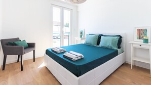 A modern bedroom with a bed, a chair, a desk, and a large window.