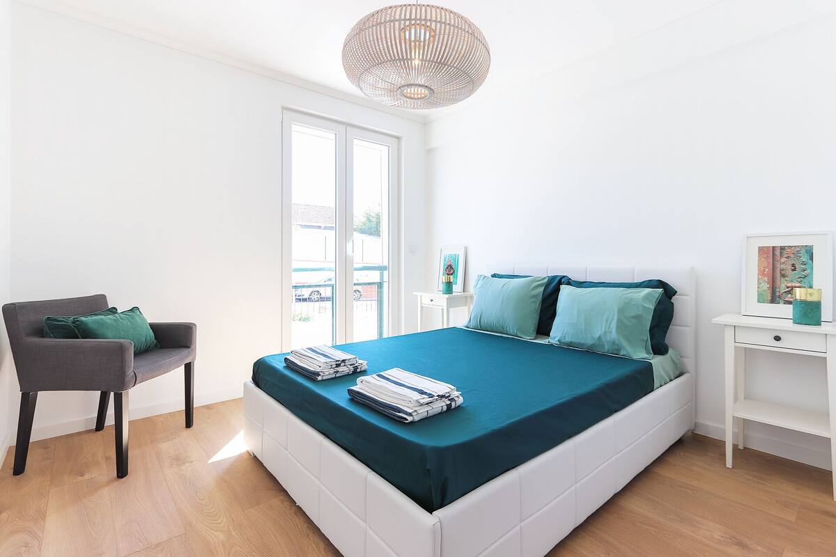 Ein modernes Schlafzimmer mit Bett, Stuhl, Schreibtisch und einem großen Fenster.