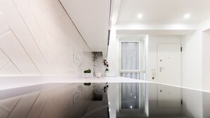 A modern, minimalist hallway with a reflective floor, a white door, and a small potted plant on a white countertop.