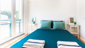 A bedroom with a large bed, two nightstands, and a view of a balcony.