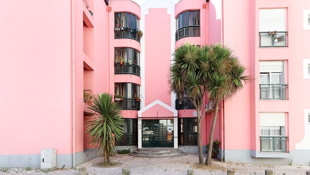A pink building with multiple balconies, a central entrance, and potted plants.