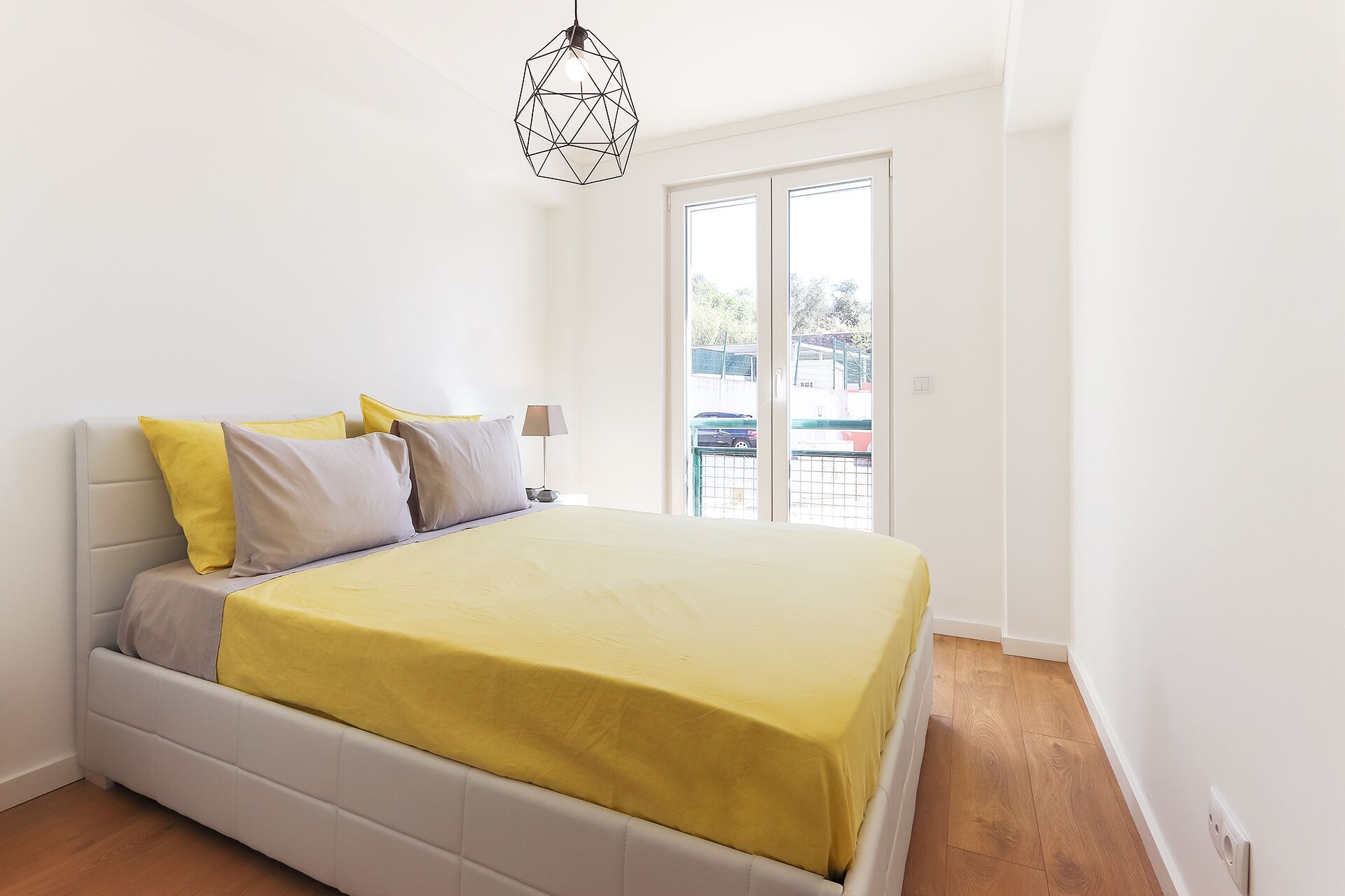 Une chambre à coucher avec un lit, des oreillers, une lampe et un luminaire suspendu aux formes géométriques.