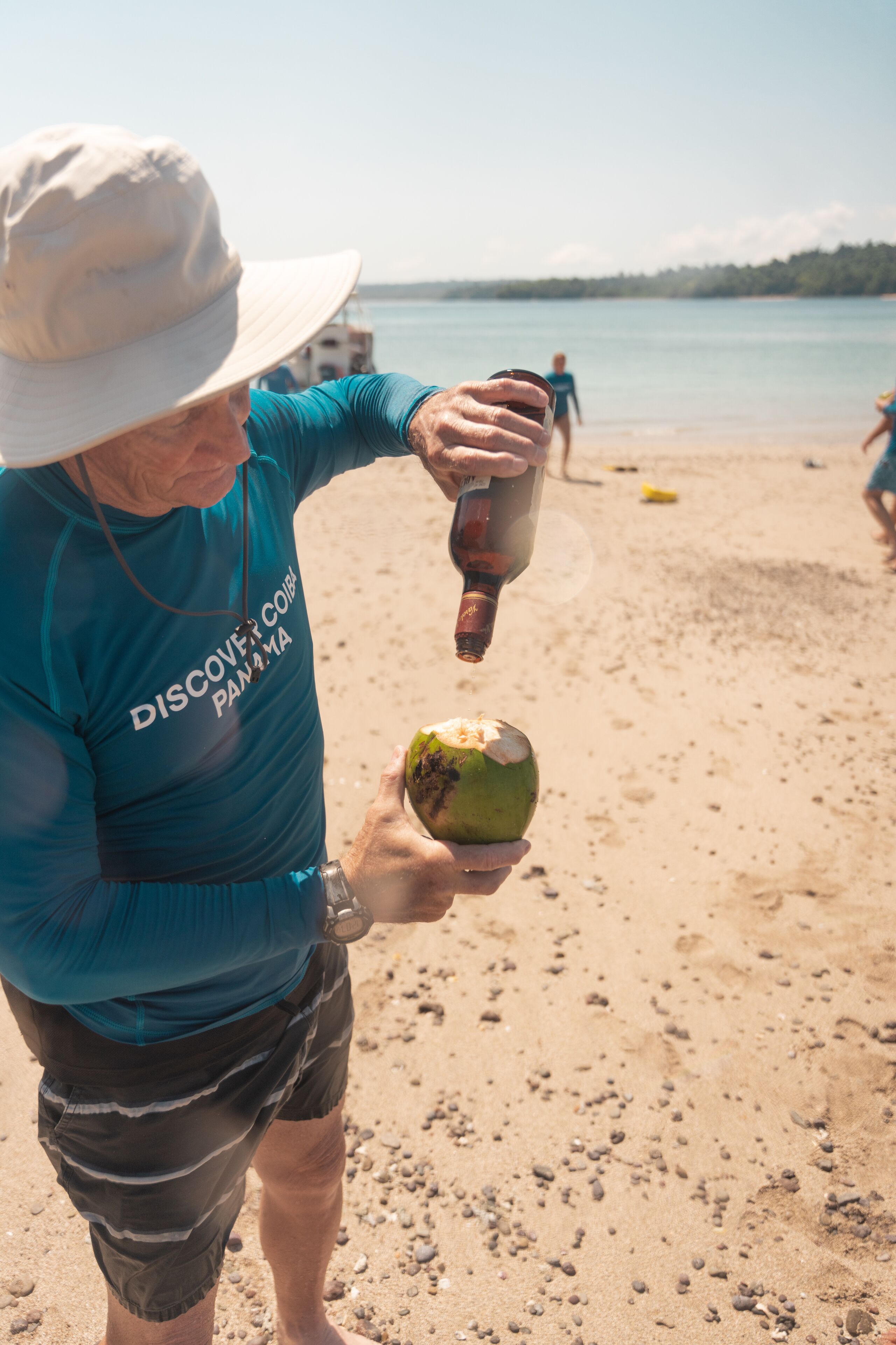 Una persona sirve una bebida de una botella en un coco sobre la playa.