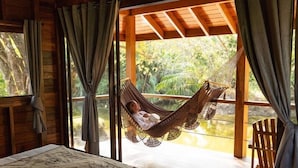 A wooden cabin with a bed, a hammock, and a view of a water body. - Catalina's Hideaway (Hicaco)