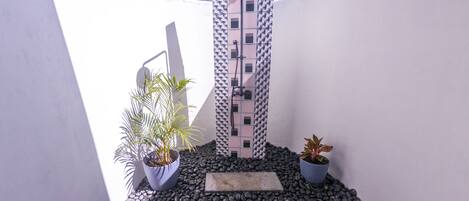 A modern outdoor shower area with a patterned wall, potted plants, and a pebble ground.