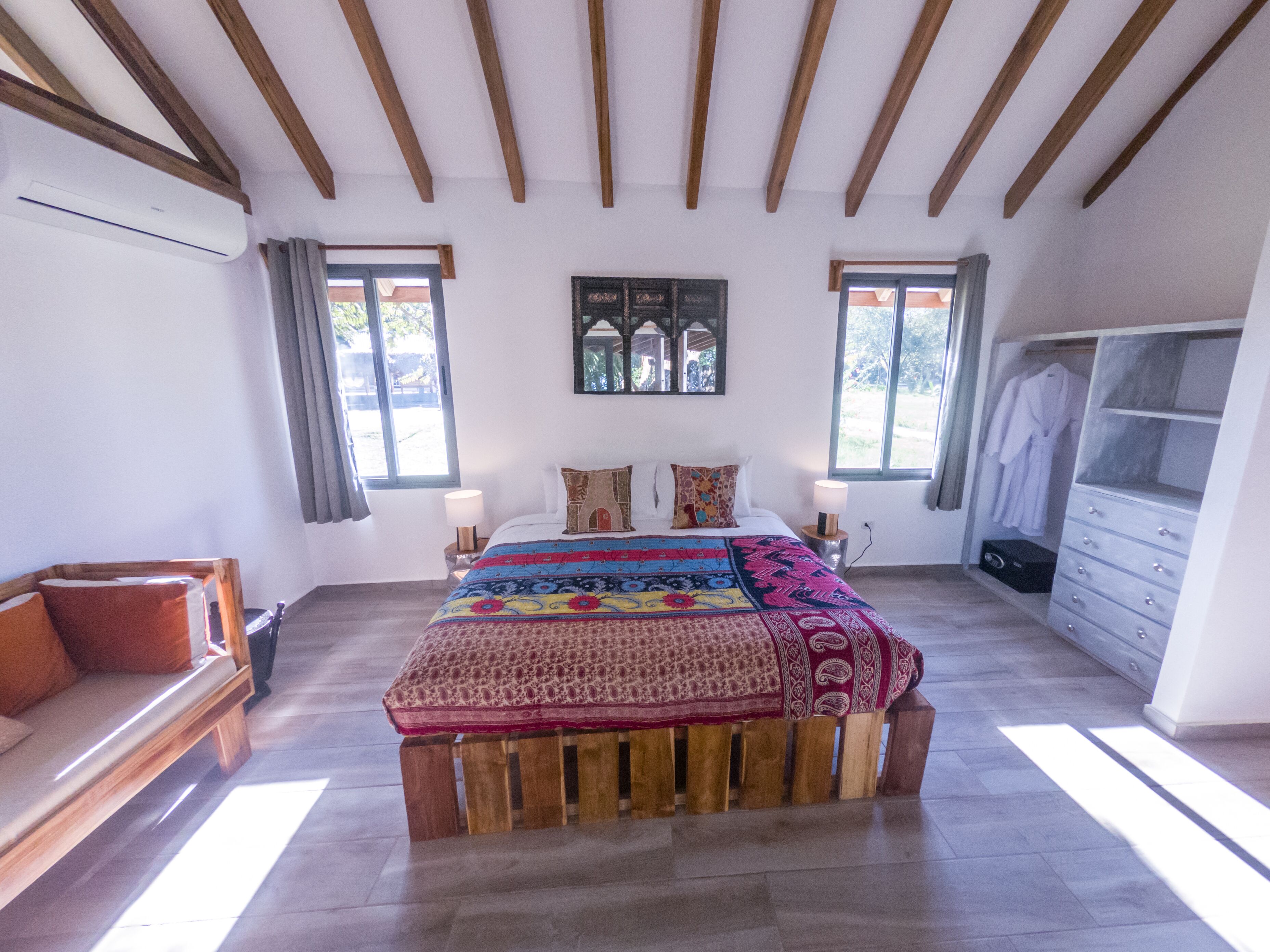 Une chambre à coucher avec un lit en bois, une table de chevet, une commode et une grande fenêtre.