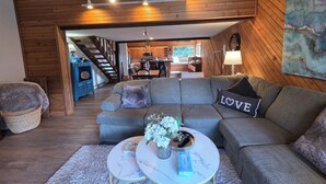 A cozy living room with a grey sectional sofa, a round coffee table with a vase of flowers, and a view into the kitchen and dining area. - Snowcreek Resort Vacation Rental 217 (Mammoth Lakes)