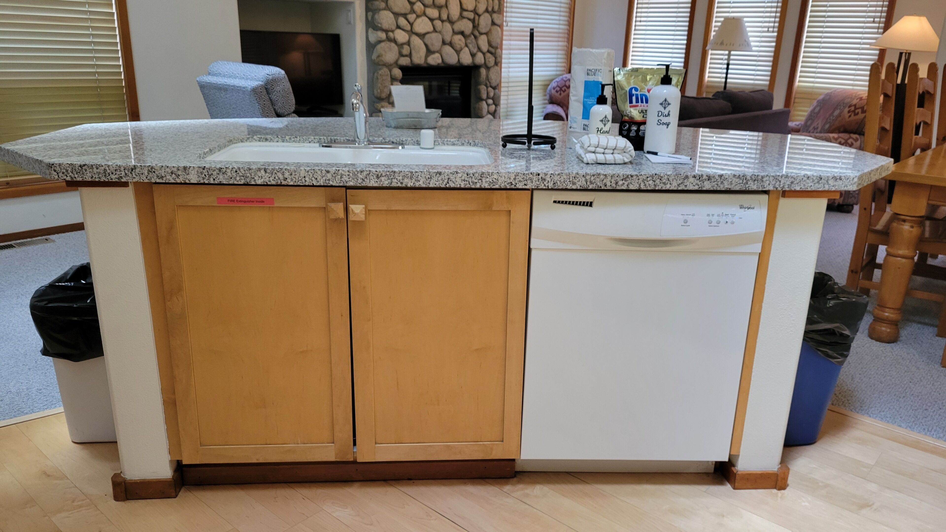 A kitchen with a built-in dishwasher, a granite countertop, and a stone fireplace.