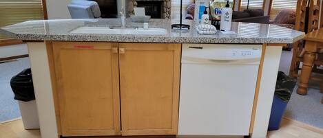 A kitchen with a built-in dishwasher, a granite countertop, and a stone fireplace.