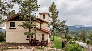 A two-story house with a red roof, surrounded by trees and mountains in the background. - Work Away From Home- Mountain Home!!! Mountain Views of RMNP,Hot Tub,Sauna, Rural, Mountain Getaway-Top Of The World, Estes Park CO (Estes Park)