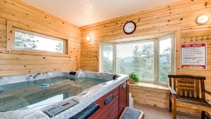 A wooden cabin interior with a hot tub, a clock, and a window with a view of trees. - Work Away From Home- Mountain Home!!! Mountain Views of RMNP,Hot Tub,Sauna, Rural, Mountain Getaway-Top Of The World, Estes Park CO (Estes Park)