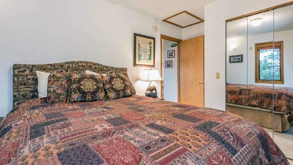 A bedroom with a large bed, a nightstand with a lamp, a framed picture on the wall, and a wardrobe.