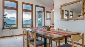 A dining area with a wooden table and chairs, large windows with a mountain view, and a tripod with a camera. - Work Away From Home- Mountain Home!!! Mountain Views of RMNP,Hot Tub,Sauna, Rural, Mountain Getaway-Top Of The World, Estes Park CO (Estes Park)