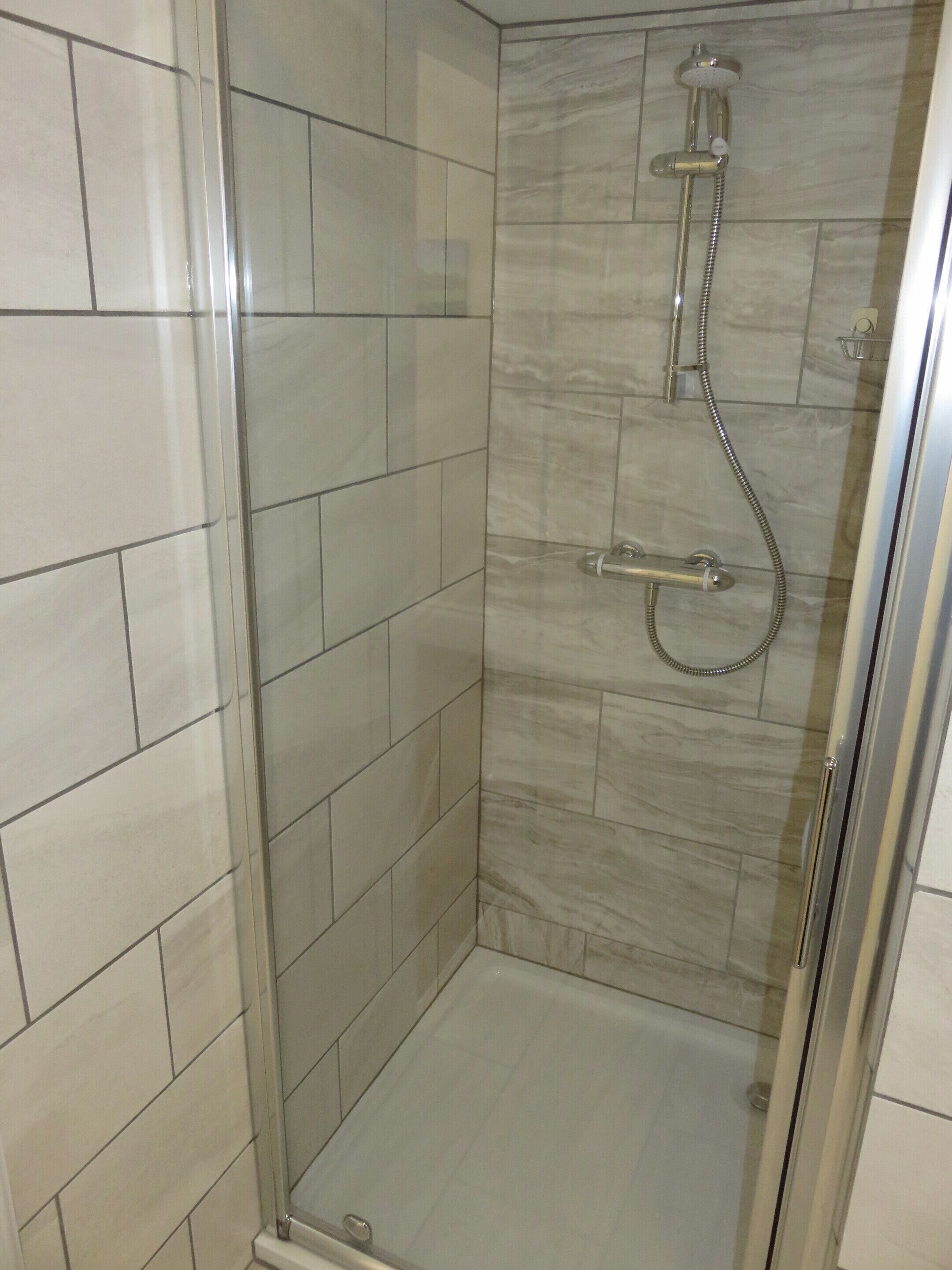 Una cabina doccia in vetro con soffione a mano e soffione fisso.