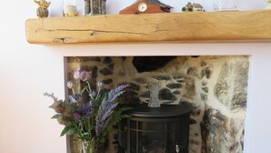 A rustic fireplace with a stone wall, a black wood-burning stove, and a shelf with various items. - Bankhouse B&B (Aberlour)