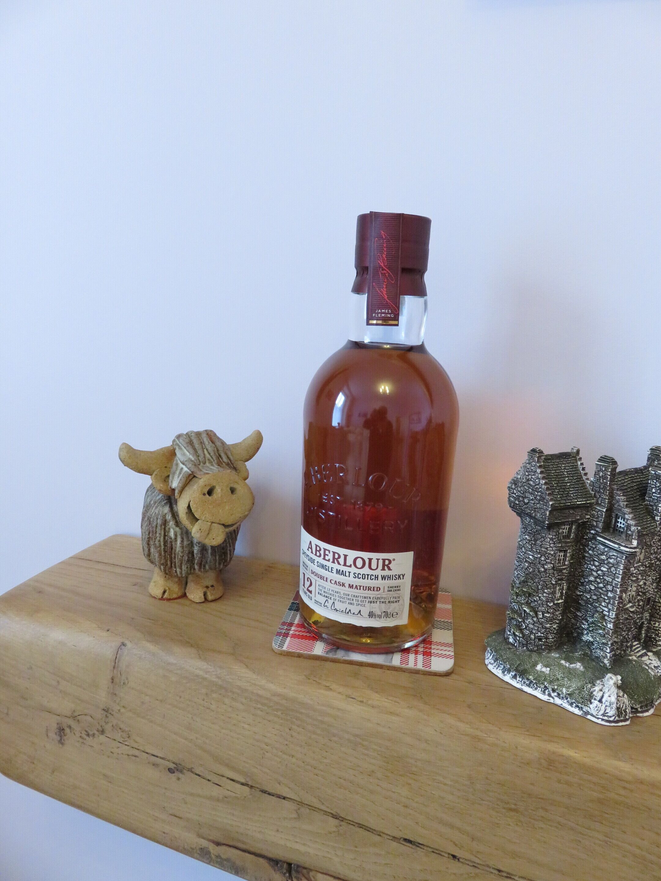 A bottle of Aberlour whisky on a wooden surface with a toy bull and a miniature castle model beside it.