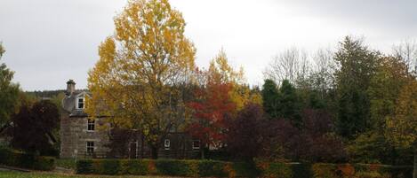 A stone building with a sign reading "The Mash Lun" in a park with autumn-colored trees and a grassy field.